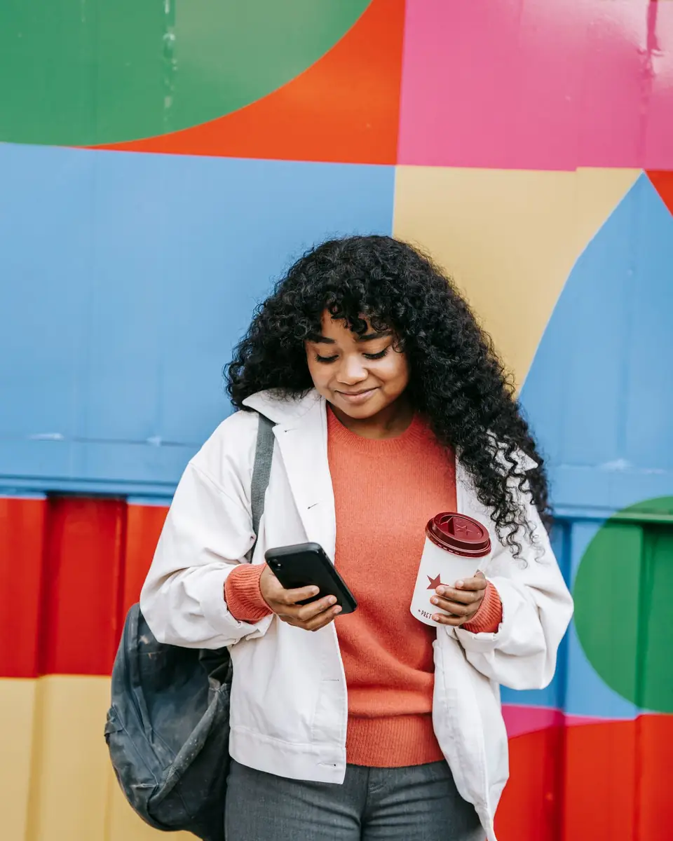 Une jeune femme regarde son téléphone devant un mur coloré.